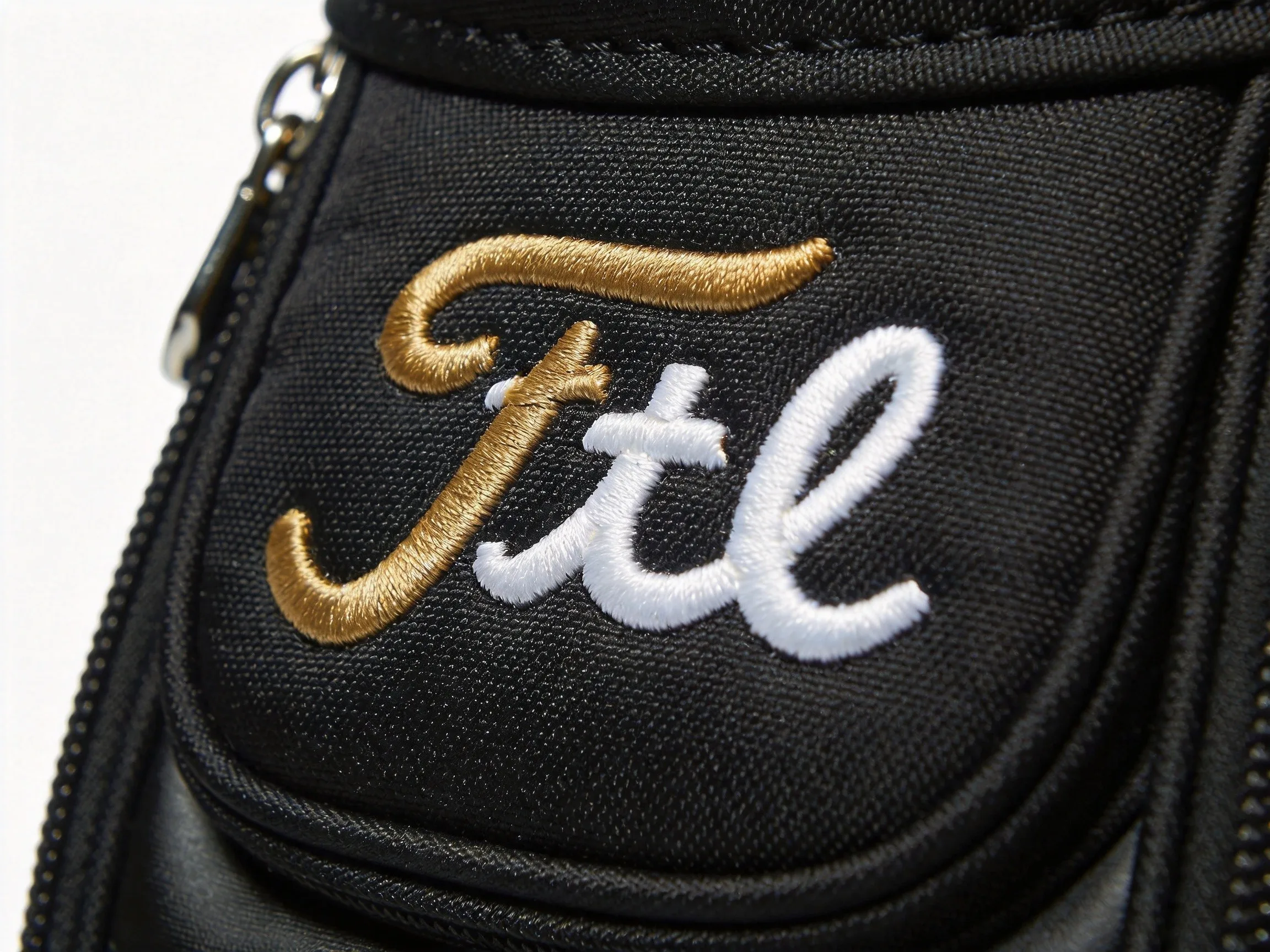 Close-up of intricate gold and white embroidered logo on black golf bag fabric showing raised thread texture and dimensional quality
